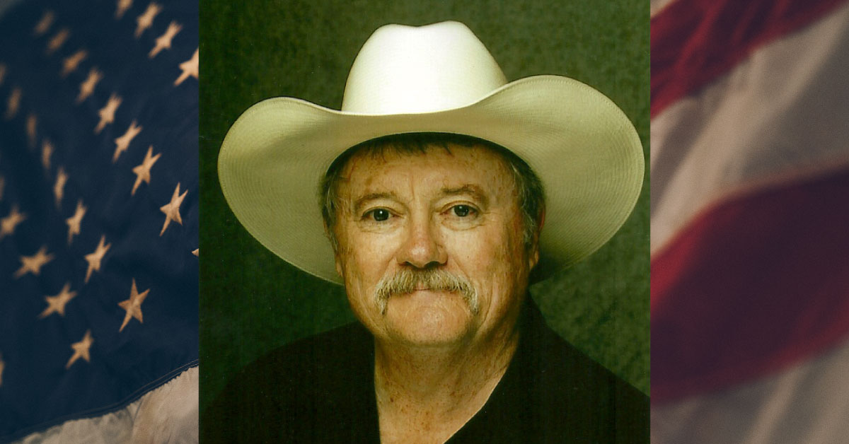 Photo of John Compere wearing a white cowboy hat, against an American flag background