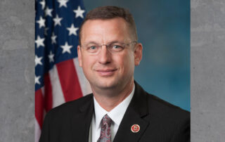 Official portrait photo of Doug Collins wearing a suit, with American flag in the background.