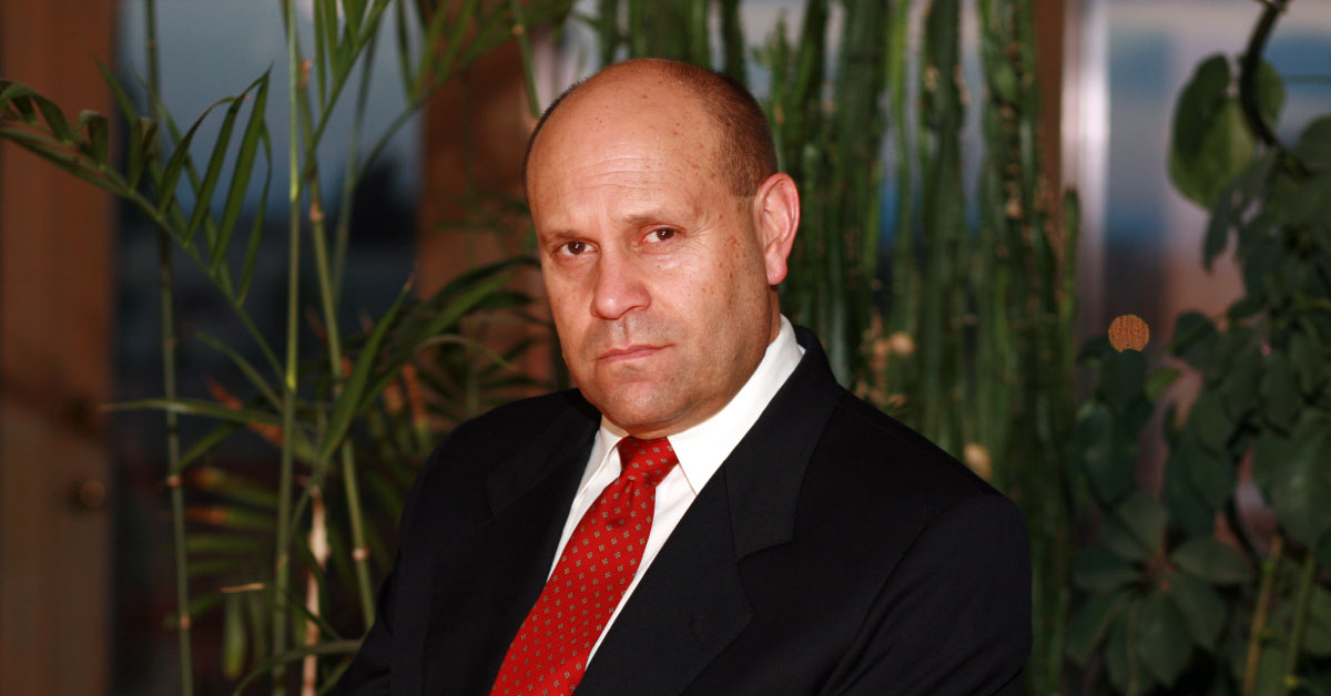 Photo of Mikey Weinstein looking intently toward the camera, wearing a black suit and red tie.