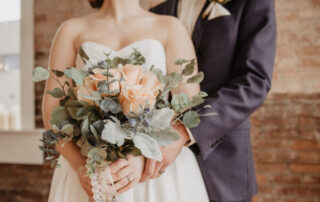 Woman wearing wedding dress holding flowers, standing in front of man wearing suit