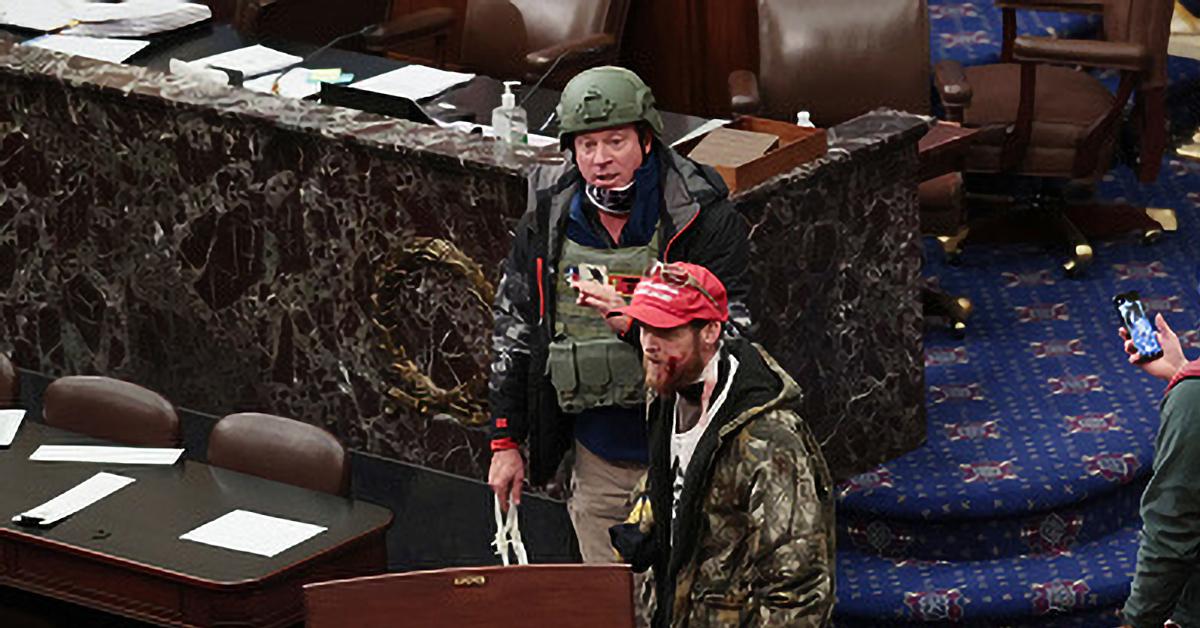 Two men wearing military style clothing and equipment standing on the floor of the US Capitol chamber.