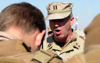 Chaplain shouting prayer at soldier whose head is bowed