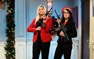 Image from Saturday Night Live sketch of Marjorie Taylor Greene and Lauren Boebert holding assault rifles with Christmas garland in the background