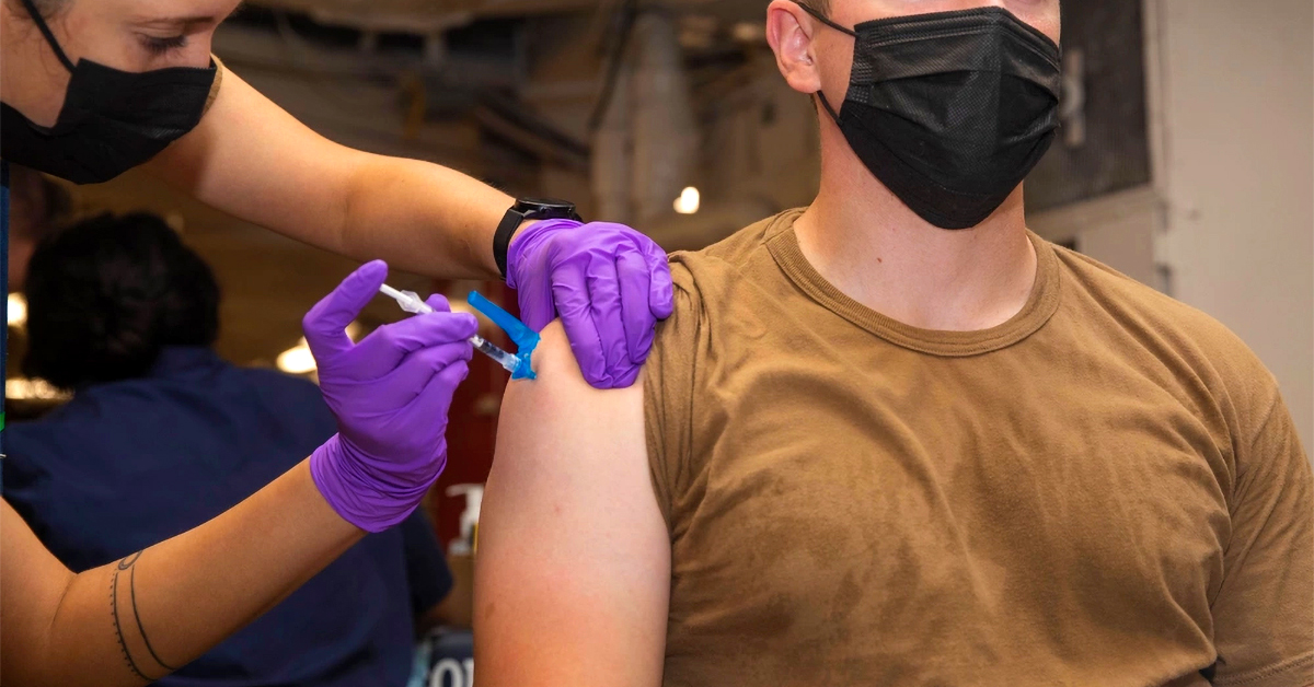 Hospital Corpsman with purple gloves administering COVID vaccine shot to another US servicemember.