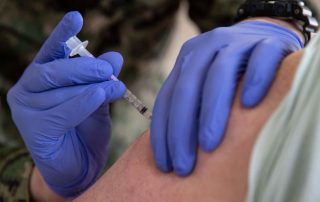 U.S. Navy servicemember administering COVID vaccine to the arm of another servicemember