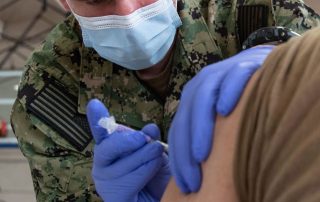 U.S. Navy servicemember administering COVID vaccine to the arm of another servicemember
