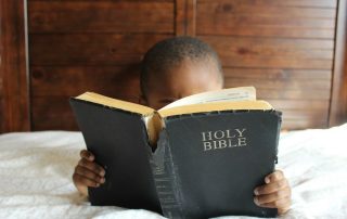 Small child reading bible that's bigger than they are