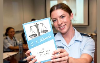 Photo of smiling female Air Force Academy cadet holding up C.S. Lewis book The Abolition of Man