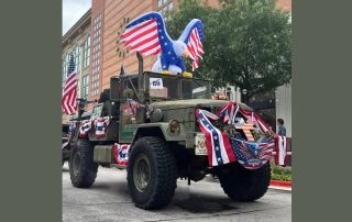 Photo of military jeep vehicle covered in 4th of July decorations one of which is a large Christian cross painted with the American flag on the front of the vehicle